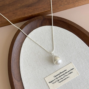 Macro view of teardrop pendant necklace with brushed silver finish on a wooden tray