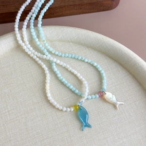Colliers de perles faits main avec pendentif poisson style océan sur un plateau beige