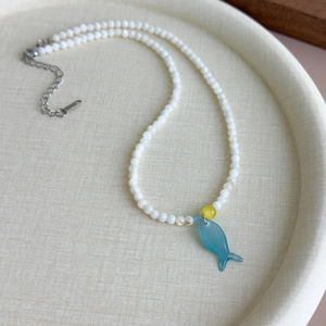 Détail du collier de perles style marin avec un pendentif en forme de poisson bleu
