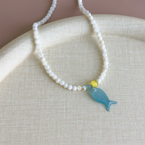 Détail du collier de perles océaniques avec pendentif poisson bleu sur tissu beige doux