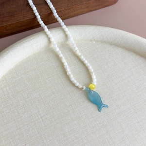 Gros plan d'un collier de perles avec pendentif poisson en verre bleu sur plateau