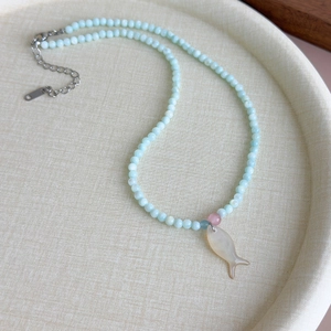 Gros plan d'un collier de perles bleu clair avec pendentif poisson sur un plateau