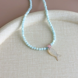 Détail d'un collier de perles bleu clair avec pendentif poisson en nacre sur plateau