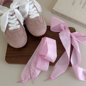 Detailed macro view of pink suede sneakers with wide white organza ribbon shoelaces