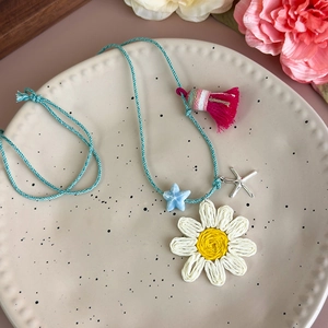 Détail du collier fleur tressée avec breloque étoile de mer et franges roses sur plateau
