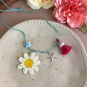 Détail du charm marguerite tissé, pendentif étoile de mer et pompon du collier de plage