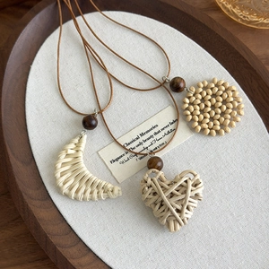 Detailed shot of woven heart, moon and sunflower pendants with wooden beads on linen fabric