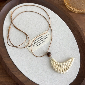 Detail of bohemian woven crescent moon pendant with brown wooden beads on long wax cord