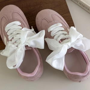 Detailed macro view of the pink suede sneakers featuring elegant white silk ribbon laces
