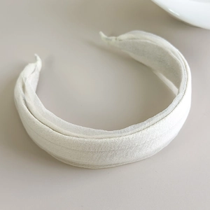 Detail of minimalist beige fabric headband with soft pleated texture on a neutral surface