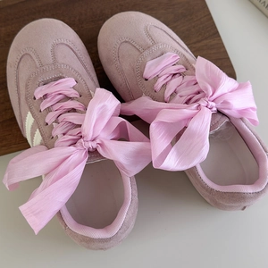 Macro shot of pink suede sneakers with wide satin ribbon laces in a ballet bow style