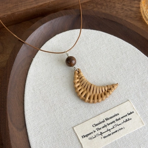 Detailed close-up of handmade woven crescent pendant with wooden bead on long cord