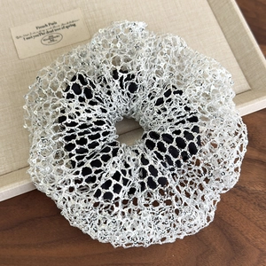 Detailed close-up of a silver sequined mesh scrunchie on a beige display tray