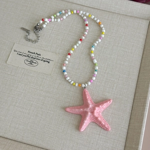 Detail of colorful beaded necklace with a textured pink starfish pendant and metal clasp