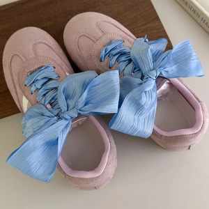 Close-up of wide blue ribbon shoelaces on purple suede sneakers with oversized bow knot
