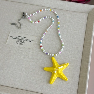 Macro detail of yellow starfish pendant with colorful beads and lobster clasp on jewelry tray