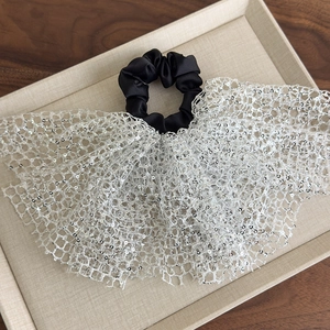 Detail of sequined mesh fabric on a black elastic scrunchie displayed on a linen tray