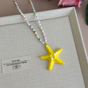 Detail of yellow starfish pendant necklace with colorful beads on a beige fabric background