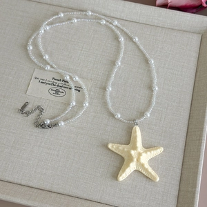 Macro shot of yellow starfish pendant with pearls and crystal beads on a beige linen box