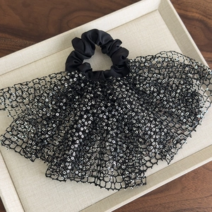 Close-up of black mesh scrunchie with silver sequins and lace on a beige tray