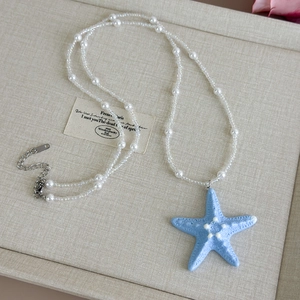 Detail of beaded pearl necklace with light blue starfish pendant and silver lobster clasp