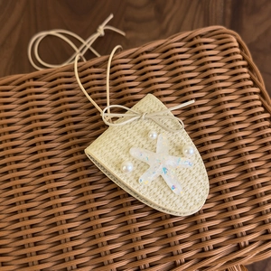 Détail du sac tissé en forme d'écu avec étoile de mer et perles sur texture d'osier