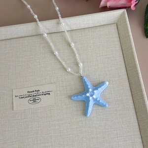 Detailed macro view of a light blue starfish pendant on a white pearl beaded necklace