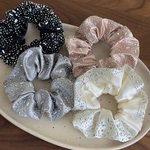 Dettaglio di elastici scrunchie in seta con strass in nero, rosa, grigio e bianco