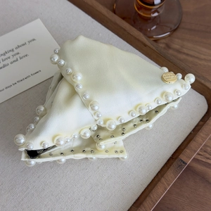 Close-up of elegant cream satin hair claw with large pearls and gold emblem detail