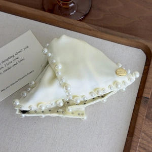 Detailed view of cream fabric hair claw clip with elegant faux pearls and gold emblem