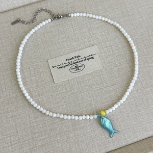 Detailansicht einer weißen Perlenkette mit blauem Fisch-Muschel-Anhänger und Silberverschluss