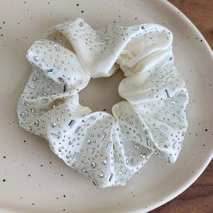 Dettaglio macro di uno scrunchie in raso crema con strass lucidi su un vassoio