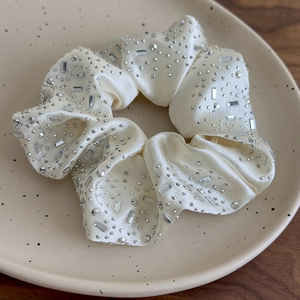 Dettaglio di scrunchie in seta color crema con strass argentati su un piatto di ceramica