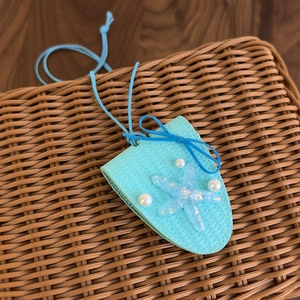 Détail d'un pendentif en cuir bleu clair avec texture tressée, étoile de mer et perles