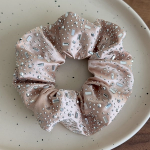 Dettaglio di un elastico per capelli in raso rosa champagne con strass in ciotola di ceramica