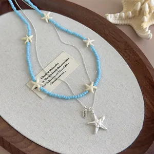 Detail of layered blue starfish beaded necklace with Lucky charm on wood tray