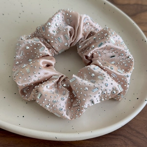 Macro di uno scrunchie in raso champagne con strass scintillanti su vassoio di ceramica