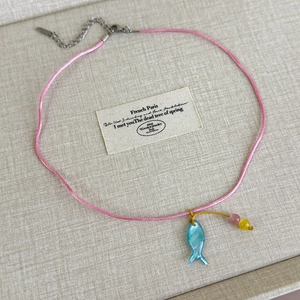 Detail einer rosa Kordelkette mit blauem Fisch-Muschel-Anhänger und bunten Perlen