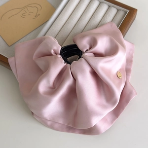 Detailed view of large pink satin bow hair claw clip with golden circular tag on soft fabric