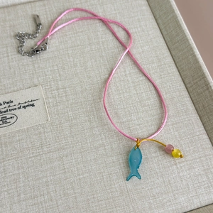 Detail einer rosa geflochtenen Kette mit blauem Fisch-Anhänger und Perlen in einer Box