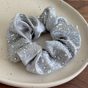Vista macro di elastico per capelli in raso grigio argento con strass lucidi su piatto ceramico