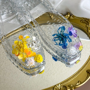 Detail shot of vibrant handmade beads and floral charms on transparent PVC sandals
