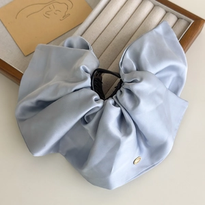 Detailed view of large blue satin bow hair claw clip with golden metal decorative tag