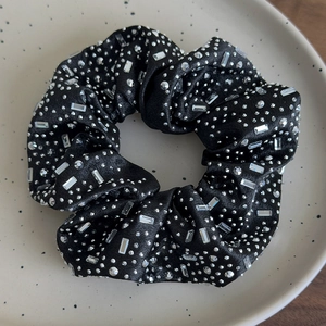 Dettaglio di elastico in raso nero con strass scintillanti su vassoio ceramico