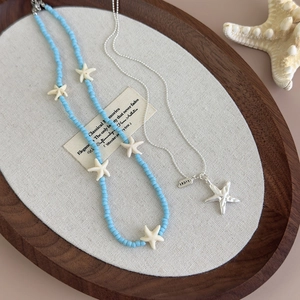 Detailed close-up of blue bead necklace with white starfish charms and Lucky tag