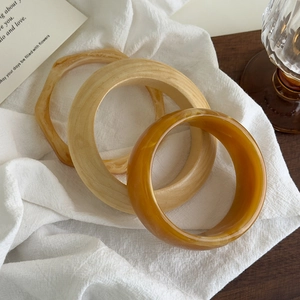 Trois bracelets en résine acrylique avec texture ambre et grain de bois sur tissu blanc