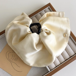 Detailed texture of large cream satin bow hair claw clip with a golden metal button