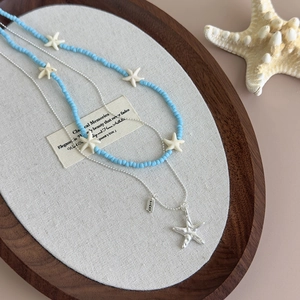 Detailed shot of double-layered blue beaded necklace and silver chain with lucky starfish charm