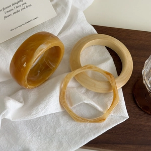 Détail de joncs en résine ambrée et bague en bois sur lin blanc et fond en bois foncé
