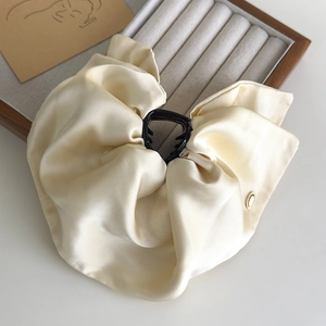 Detail of elegant cream satin bow hair claw clip with golden metal buckle and glossy finish